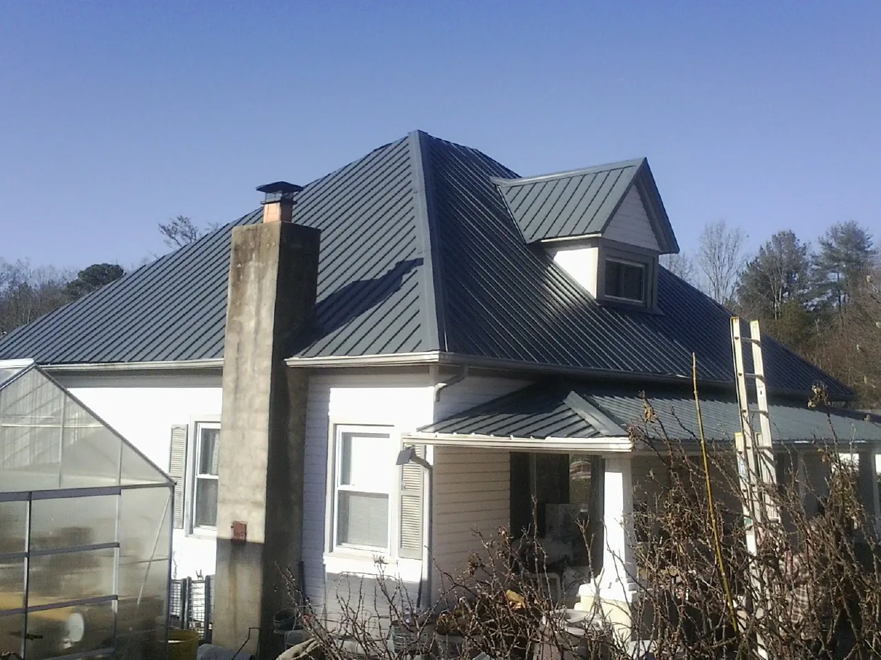 Dark blue standing seam metal roof on a white farmhouse with dormer — Slate & Tile Roof Repair by Roofing Brothers in Vassar