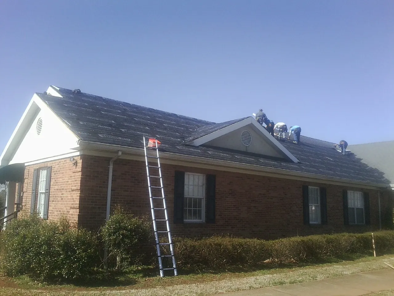 Crew tearing shingles off a brick ranch roof with a ladder set — Emergency Roof Repair work by our crew in Vassar