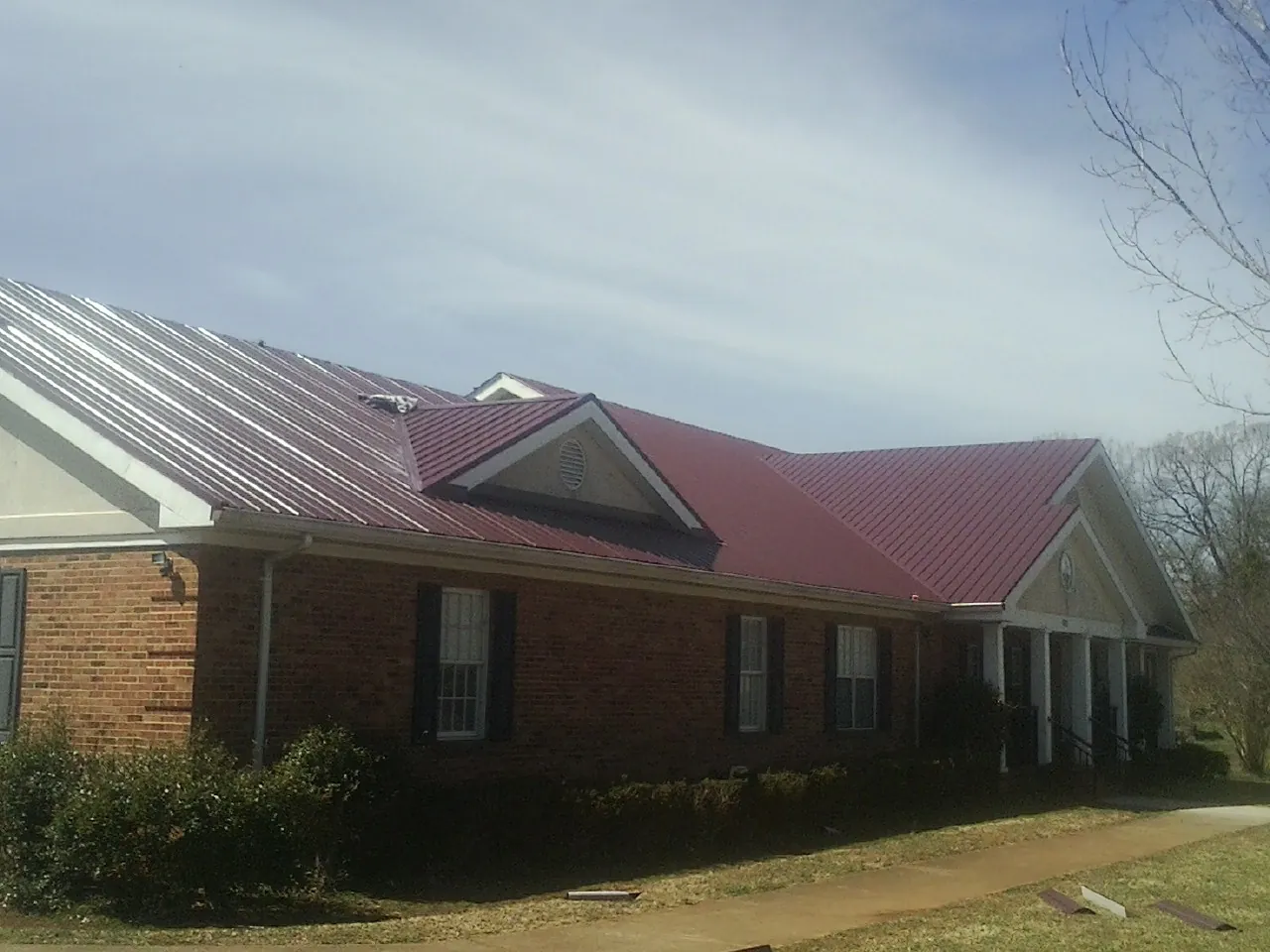 Red metal roof with gabled entries on a long brick building, from a Hail Damage Roof Repair job in Vassar