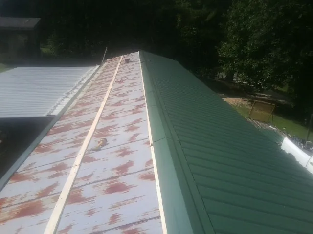 Old rusted panels beside newly installed green metal roofing — Wind Damage Roof Repair by Roofing Brothers in Vassar