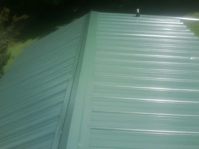 New green metal panels meeting at the ridge of a roof — Flat Roof Repair work by our crew in Vassar