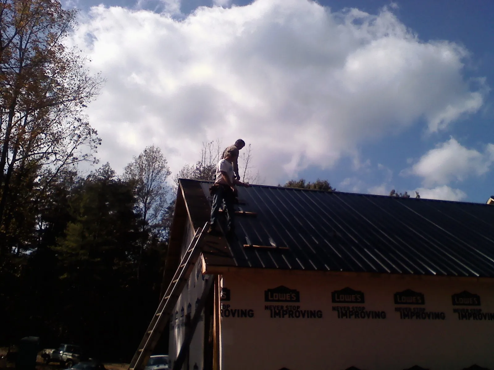 Roofer fastening dark metal panels high against a cloudy sky, from a Roof Inspection job in Vassar