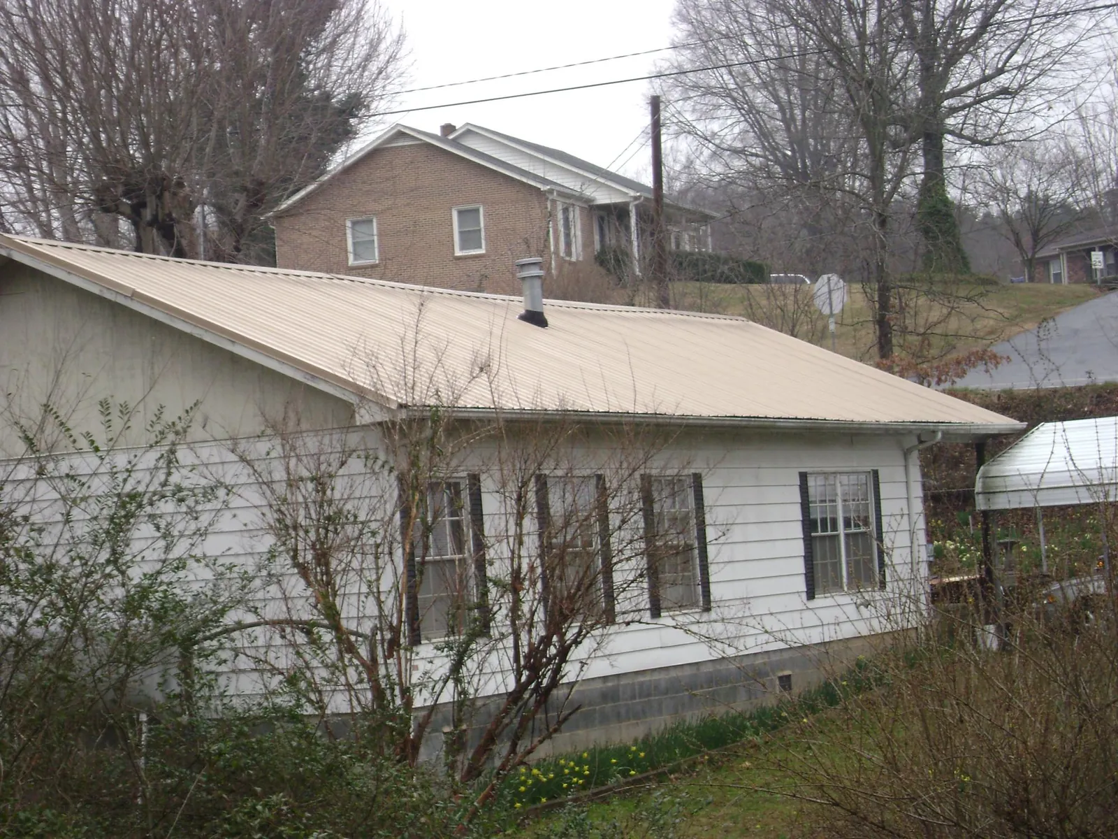 Tan metal roof on a white sided house set into a hillside — Commercial Roofing by Roofing Brothers in Vassar